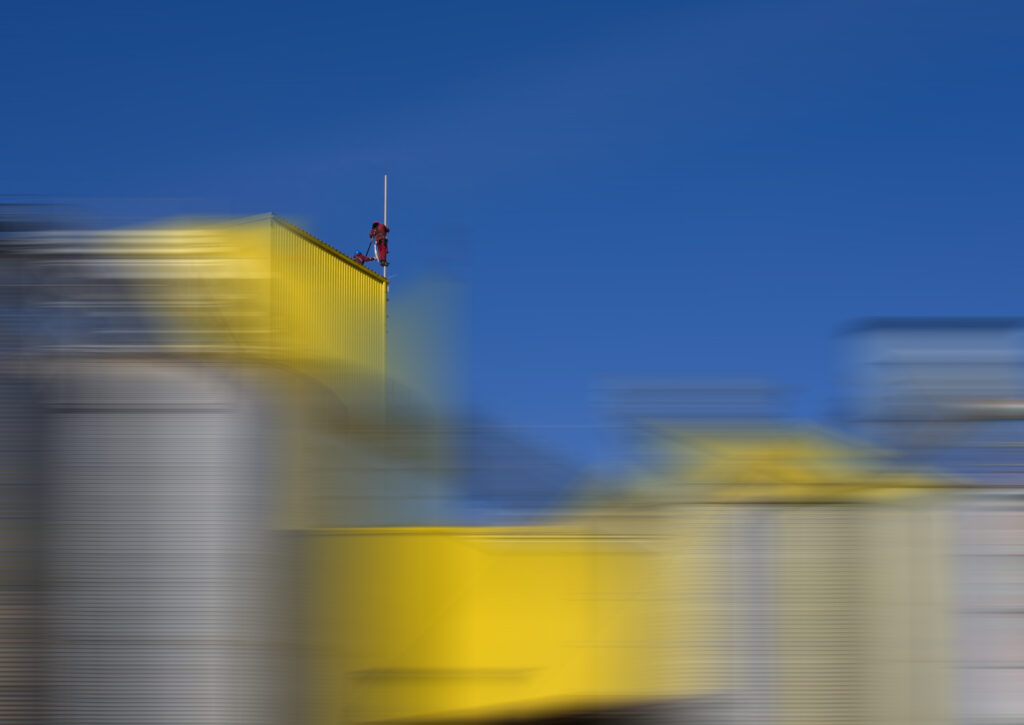 Technician in safety gear standing on a yellow container at an outdoor field testing site.