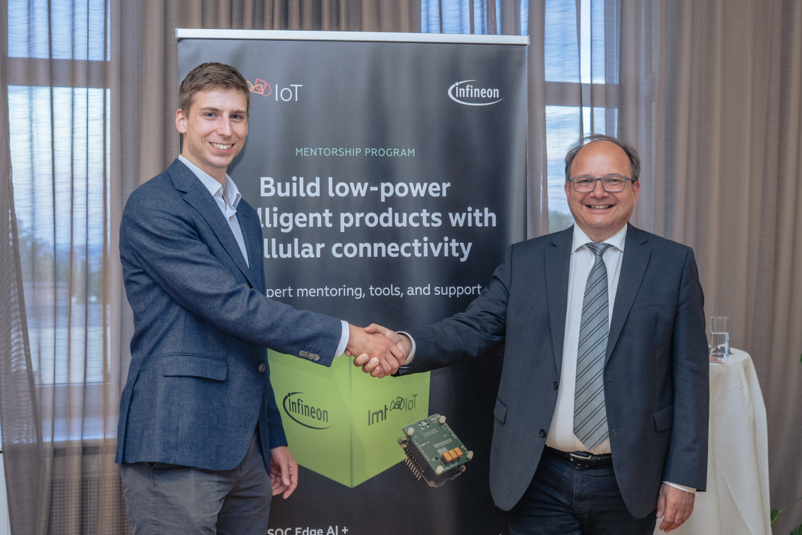 LMT IoT representative Reinis Skorovs shaking hands with Infineon Technologies representative Andreas Muehlberg at the launch of a low-power Edge AI and cellular IoT mentorship program in Vienna.